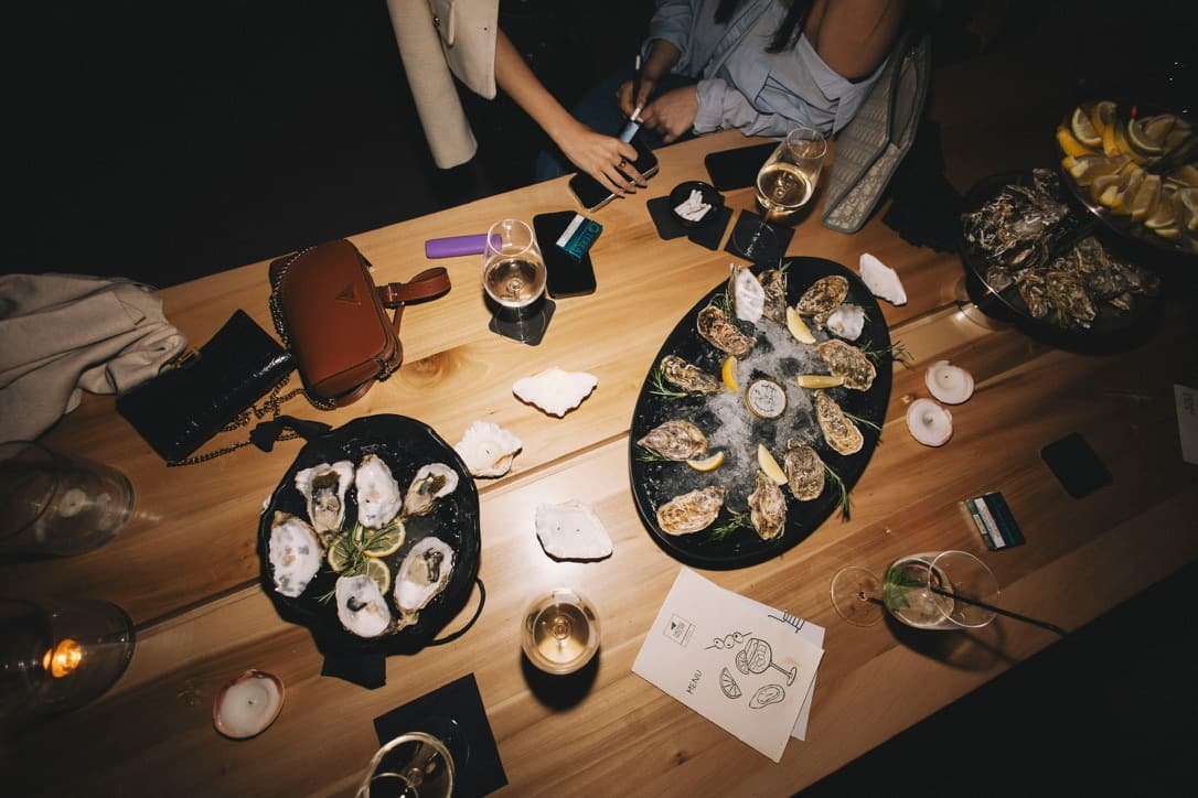 Two oyster platters on a wooden table surrounded by guests at a TheVtaste event