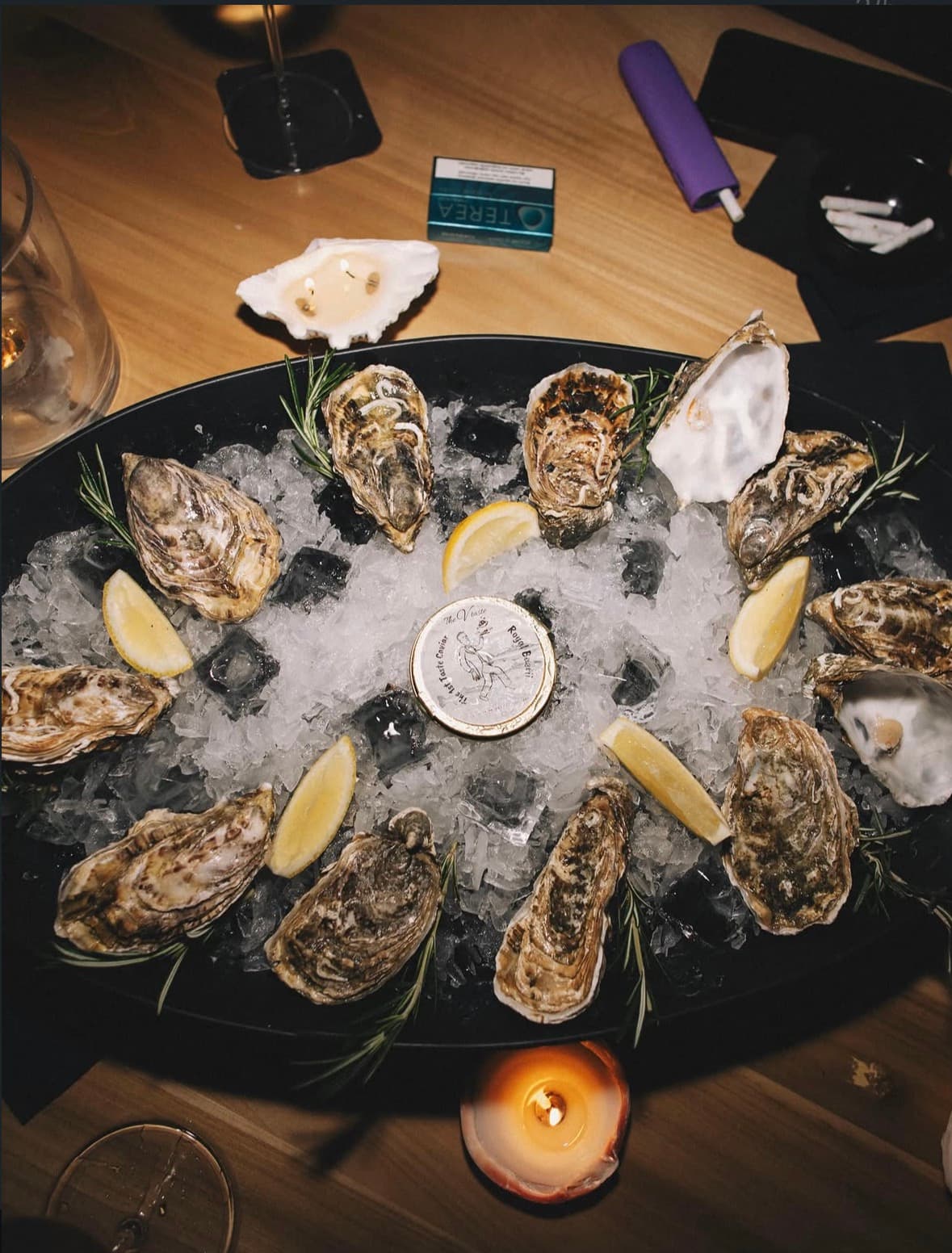 An overhead view of a TheVtaste oyster platter on ice, lit by candlelight